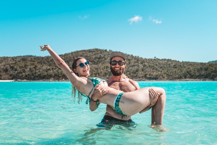 Two people with their hands in the air at Whitehaven Beach, Swimming in the Whitsundays