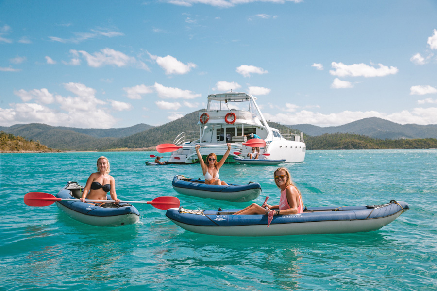 Three women in kayaks infront of a catamaran