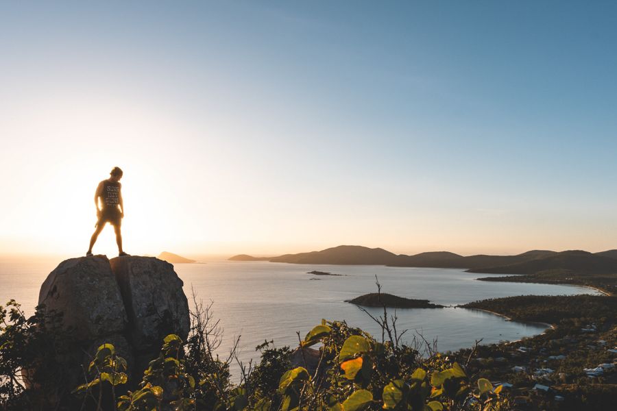 person standing on a rock near the ocean at sunrise