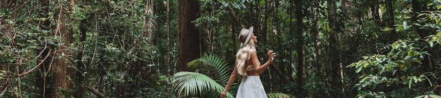 A girl in a white dress and hat walking through a rainforest