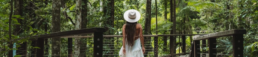 A girl walking through a rainforest wearing a white hat and dress