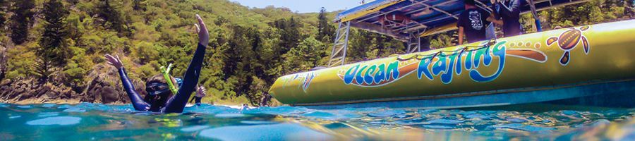 Person snorkelling with their hands raised in the air, Ocean Rafting anchored in the background