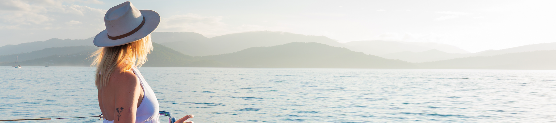 A woman in a white hat standing on a boat looking at the sunset