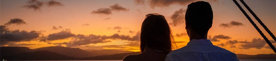 A couple with their backs facing the camera looking out at a sunset