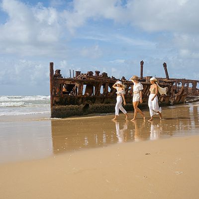 three travellers walking past maheno shipwreck on k'gari