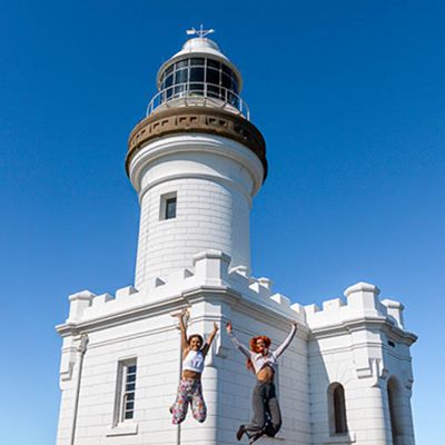 The Byron Bay lighthouse with two people jumping high in front of it