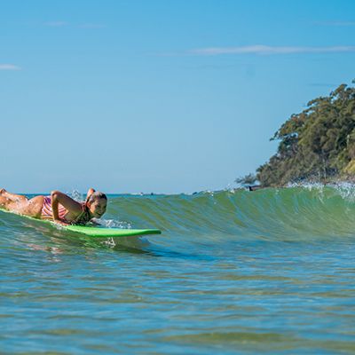 Woman on a green surfboard about to pop up on a small, clear wave