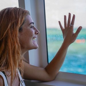 A girl with red hair smiling out the window of a boat with her hand on the glass