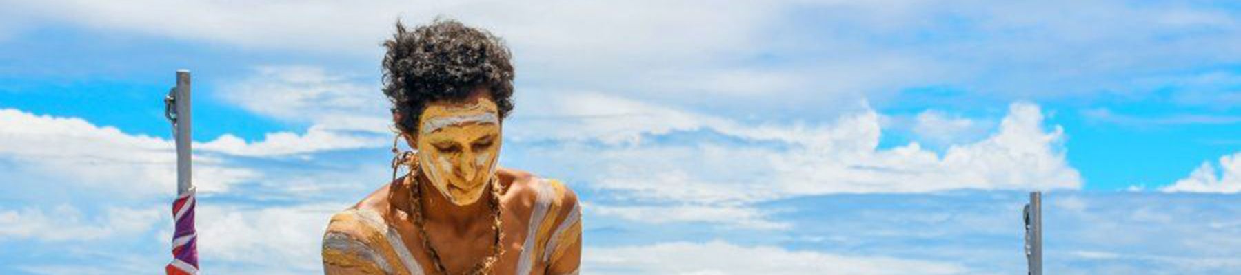 Indigenous man with traditional paint on board standing near the reef