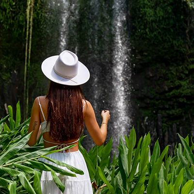 Woman in a white dress looking at Millaa Millaa Falls, surrounded by forest greenery