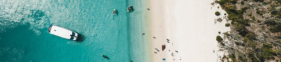 Aerial image of Whitsunday Bullet anchored in the Whitsundays, guest paddleboarding in the shallows