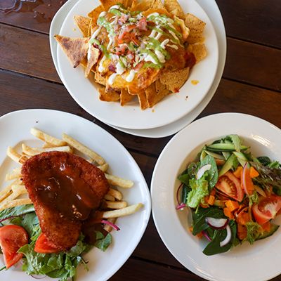 Three plates of pub food, nachos, parmi and salad