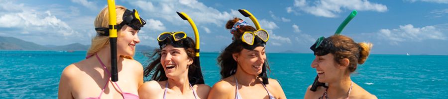 four girls with snorkel gear smiling on a boat tour in cairns