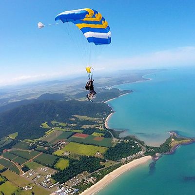 person skydiving over blue seas, white beaches and green land.