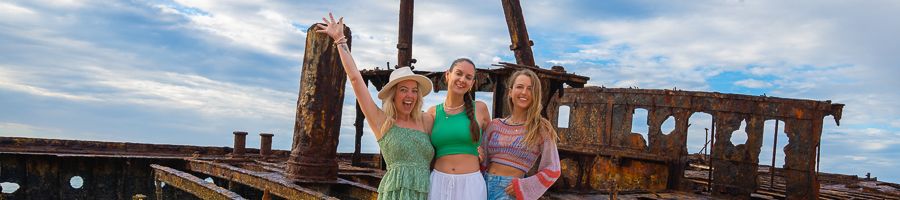 three people posing in front of maheno shipwreck