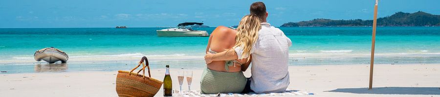 A couple sitting on Whitehaven Beach with a champagne picnic and Salty Yacht in the background