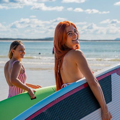 Two women with surf boards in the sun on the beach