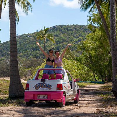 Magnetic Island little 4WD with two people smiling out the top near palm trees
