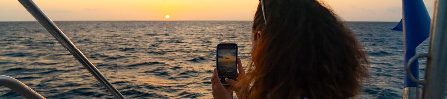 woman taking a photo of the sunset on a boat