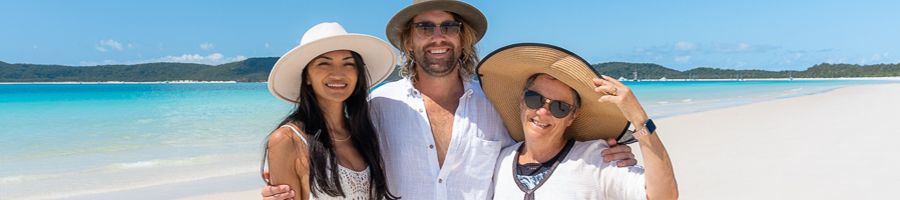 Three people at a beach with white hats on smiling