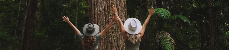 Two girls wearing hats throwing their arms in the air in a rainforest