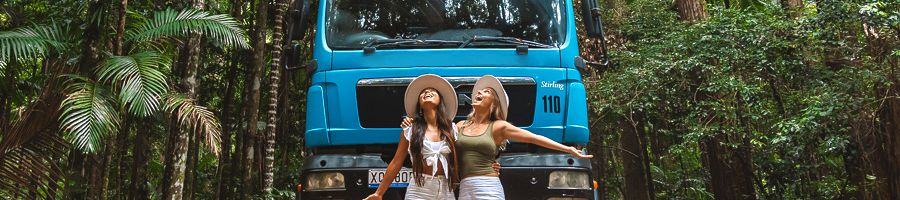 Two women in the forest of K'gari in front of a blue bus