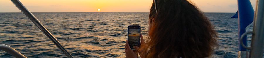 girl taking a photo of the sunset at sea