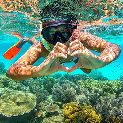 Man snorkelling in the Great Barrier Reef holding a heart sign