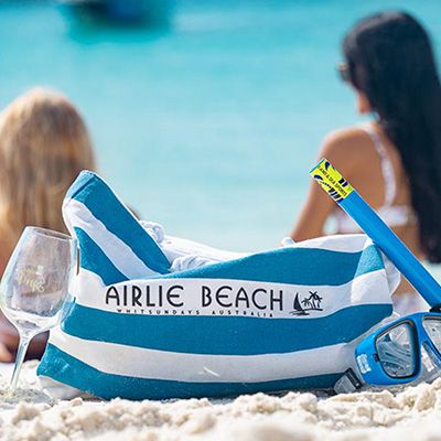 A bag that reads Airlie Beach sitting on a beach