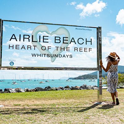 Airlie Beach sign with woman in a hat looking at ocean