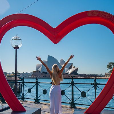 Woman standing in a heart photo frame with arms up at the sydney opera house