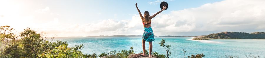 A girl standing on a hill waving her arms up in the air