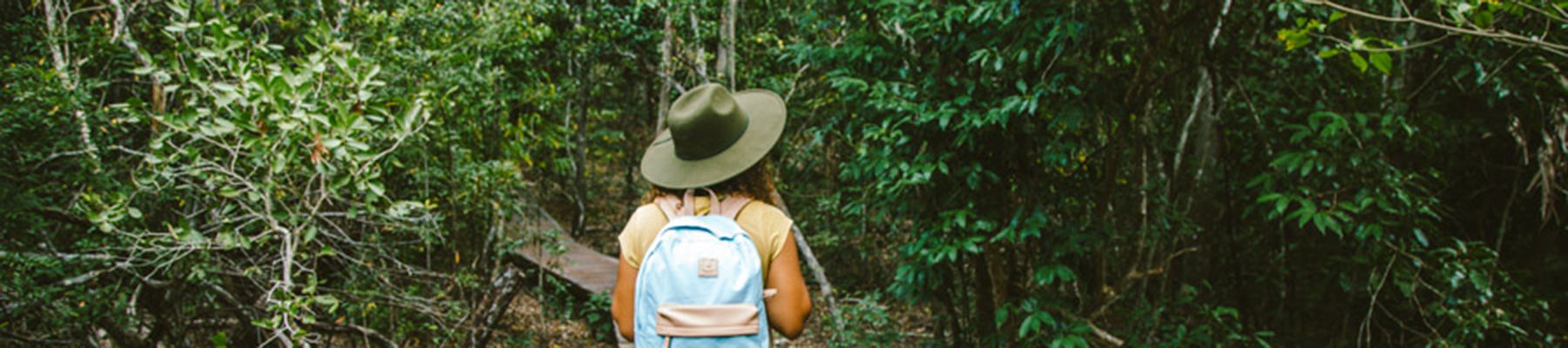 woman walking through a rainforest on a boardwalk with a backpack