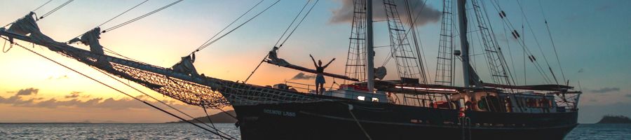 Person standing aboard Solway Lass at sunset with their arms raised
