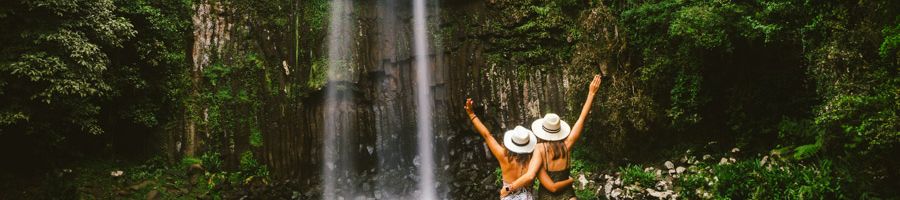 Two people wearing hats with their arms raised standing in front of Millaa Millaa Falls, Cairns