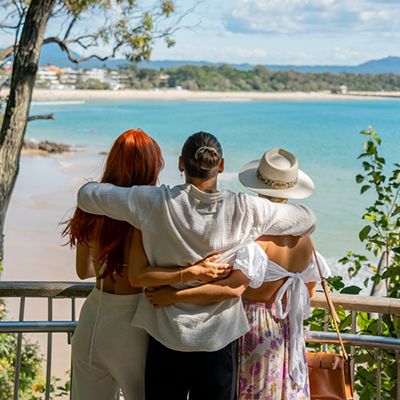 Three people with their arms around each other looking out at Noosa Beach