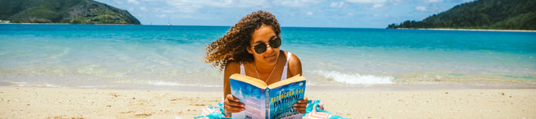Girl reading a book with sunglasses on the beach