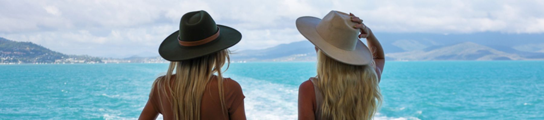 Two women holding their hats onboard a ferry cruise