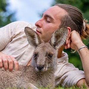Man hanging out with a kangaroo laying on the grass