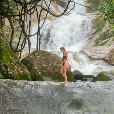 A girl walking along the rocks with a waterfall behind her