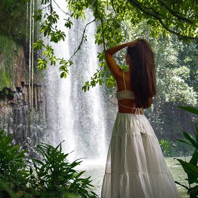 A girl standing in a dress in front of a waterfall