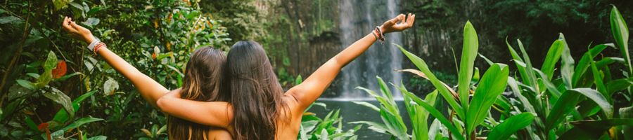 Two friends hugging with their arms raised at Millaa Millaa Falls, Cairns.