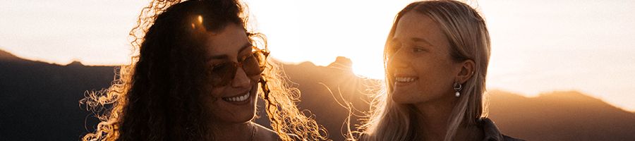Two women wearing sunglasses, sunset in the background