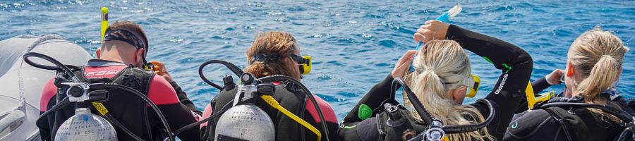 Four people sitting on the edge of a boat where scuba diving gear