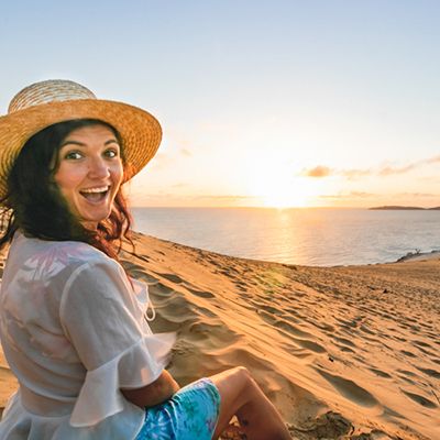Person in a straw hat smiling by the Carlo Sand Blow at sunset