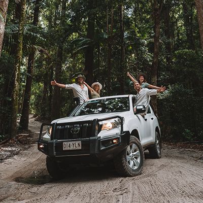 A group of backpackers in a white 4WD in a K'gari forest