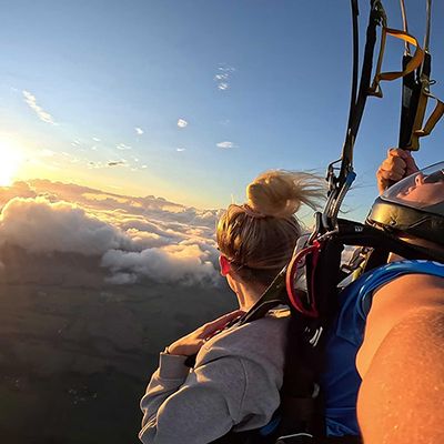 A woman and a skydive master at sunrise over the clouds