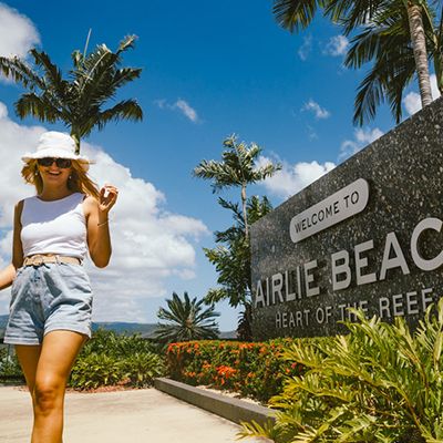 Woman in a white hat standing by the Airlie Beach sign