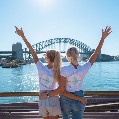 Two people in East Coast Tours shirts in front of the Sydney Harbour Bridge