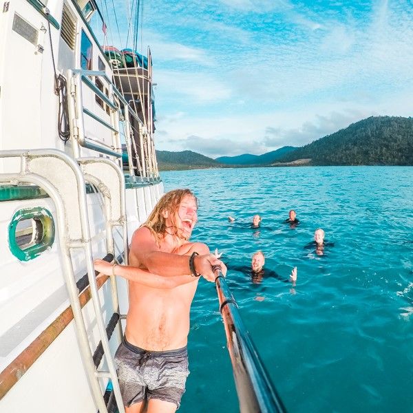 Man hanging off boat taking selfie with mates in water